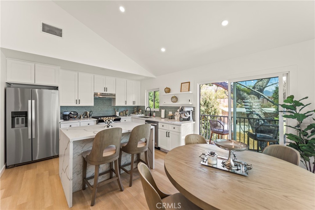 Bright kitchen with white cabinetry, marble island, stainless appliances, and dining table beside sliding glass doors.