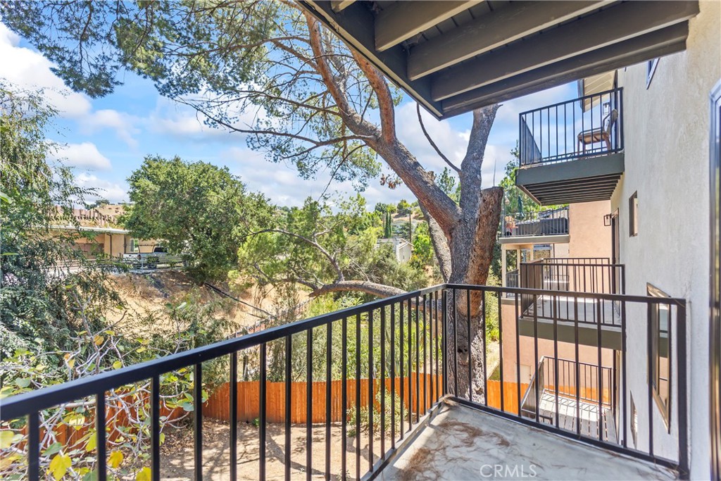 Apartment balcony overlooking a mature tree and leafy, fenced hillside.