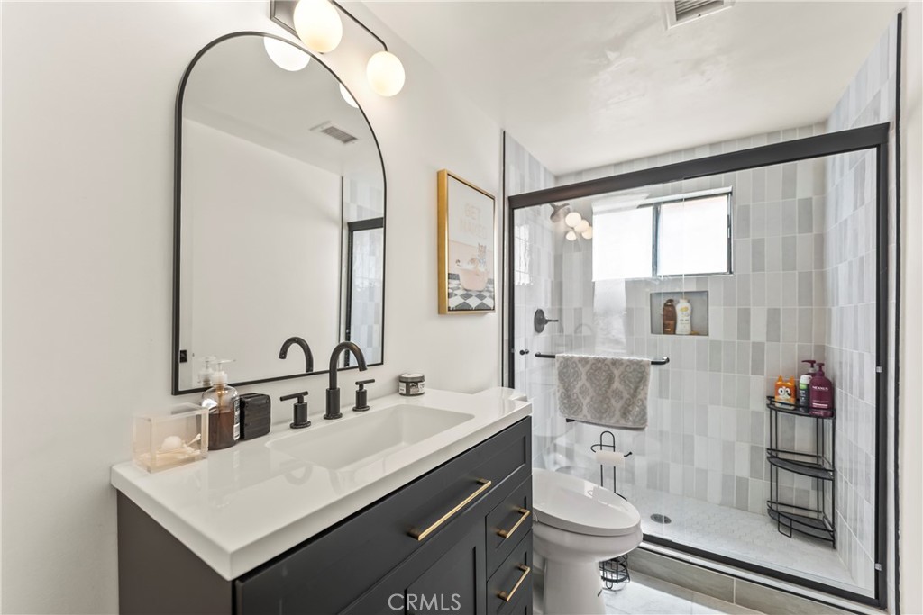 Bathroom with a dark vanity and arched mirror beside a black-framed tiled shower.