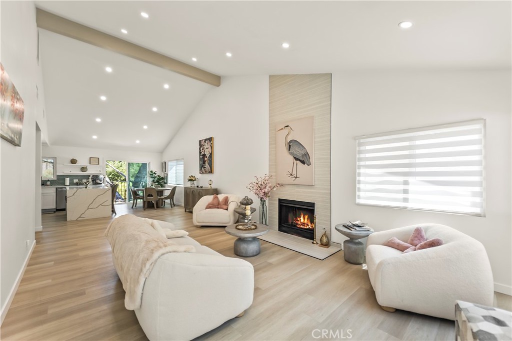 Open-plan living room with vaulted ceiling, fireplace, white seating, and kitchen and dining area beyond.