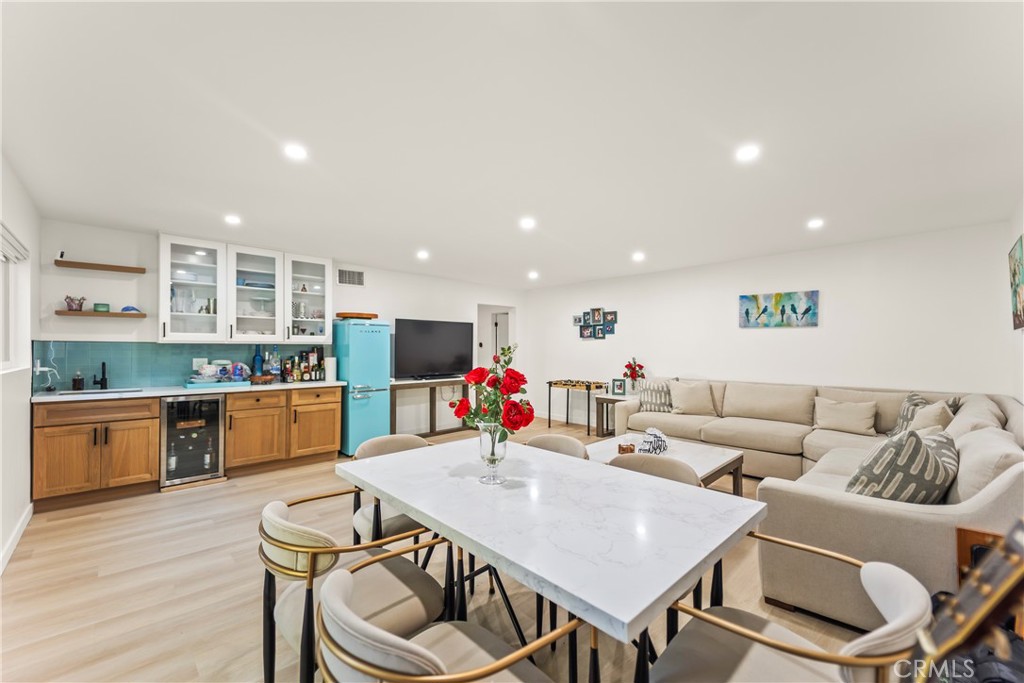Open-plan living and dining area with a white table, beige sectional, and compact turquoise-accented kitchen.