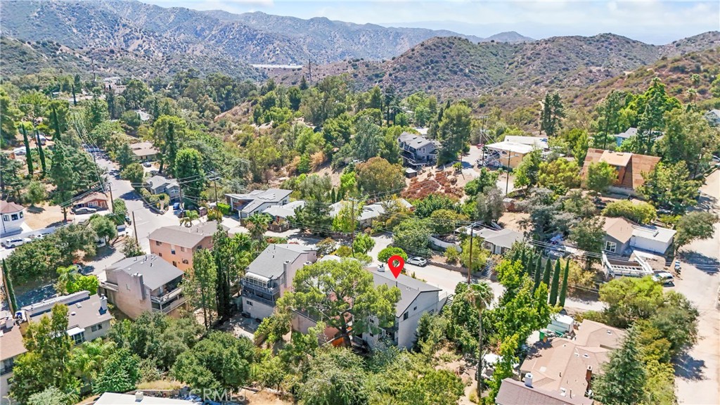 Aerial view of a home marked by a red pin, surrounded by trees and foothill homes with mountains beyond.