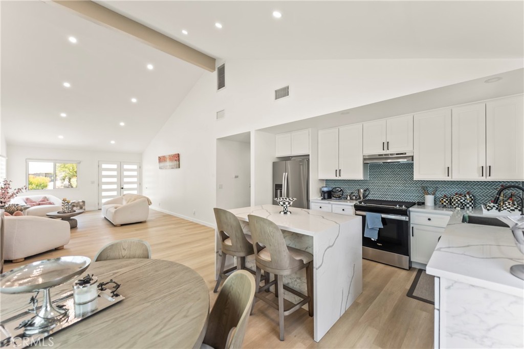 Open-plan kitchen and living area with a blue herringbone backsplash, marble-look island, and vaulted ceiling.