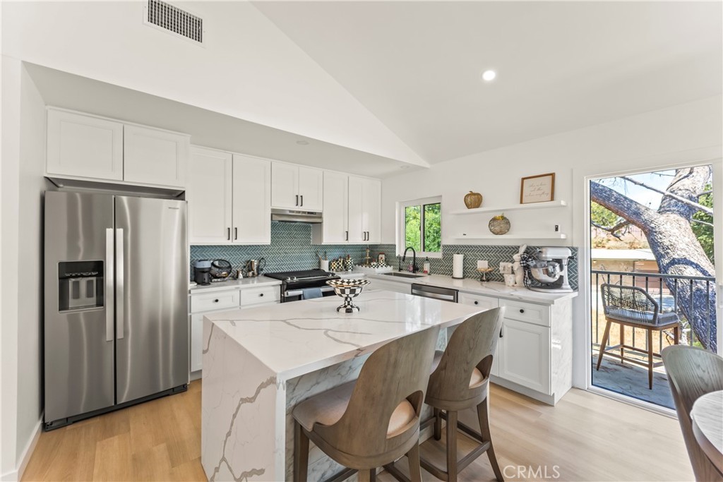 Bright kitchen with white cabinets, stainless appliances, patterned backsplash, and a large island beside a balcony door.