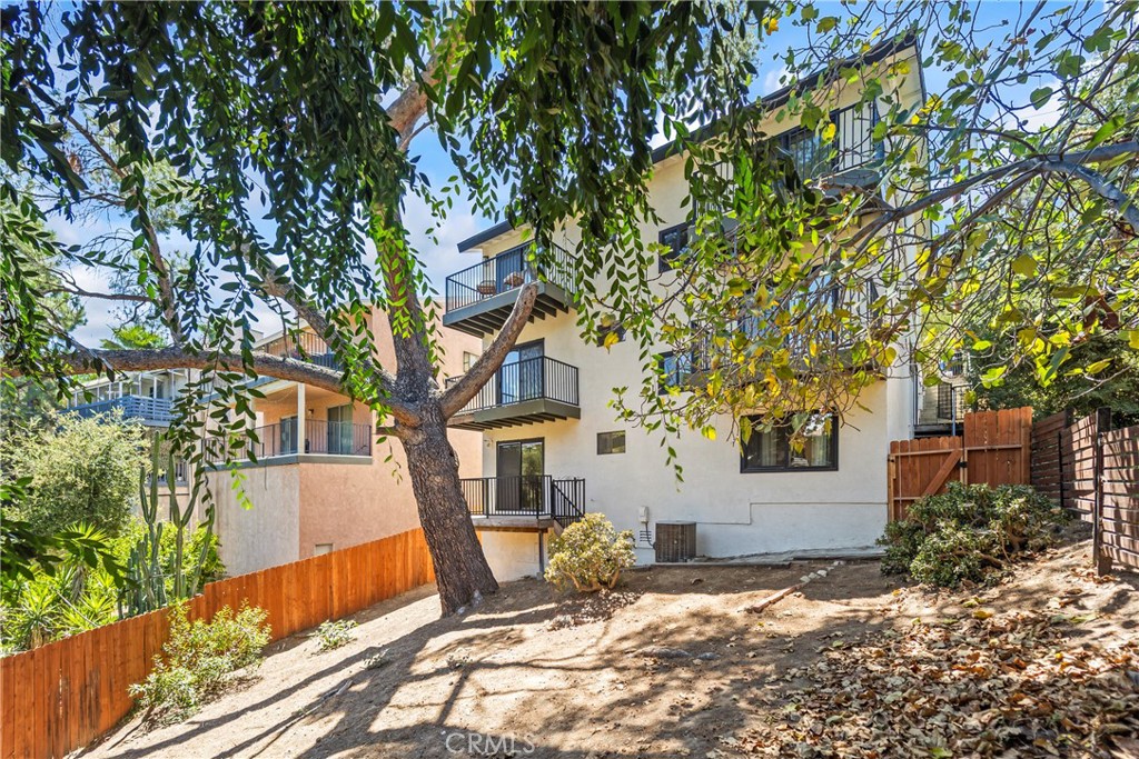 Multi-story home's rear exterior with balconies, a large leafy tree, and a sloped backyard.
