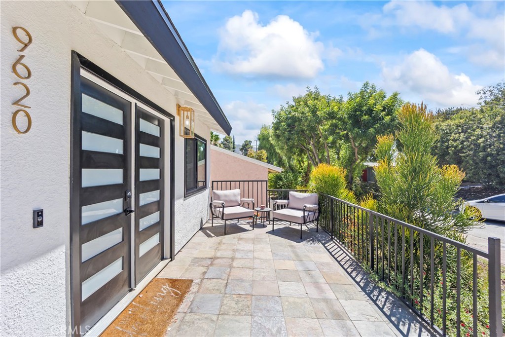 Front entry patio with black-and-glass double doors, tiled paving, and two outdoor chairs.