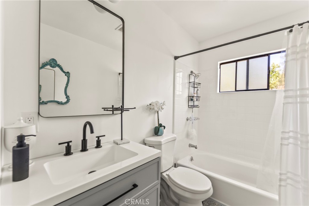 Bathroom with a gray vanity, black fixtures, and a white tub beneath a black-framed window.