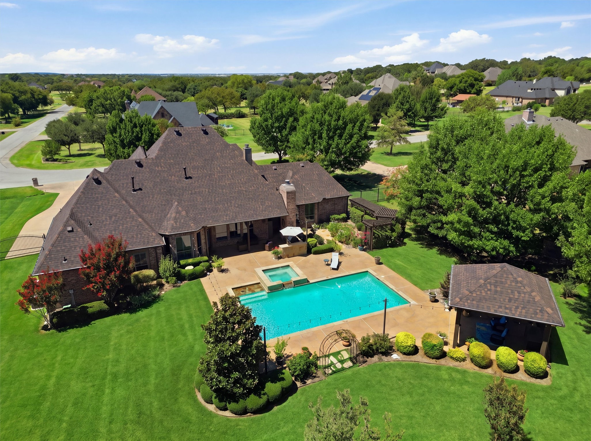Aerial view of a brick home with a backyard pool, raised spa, and landscaped lawn.