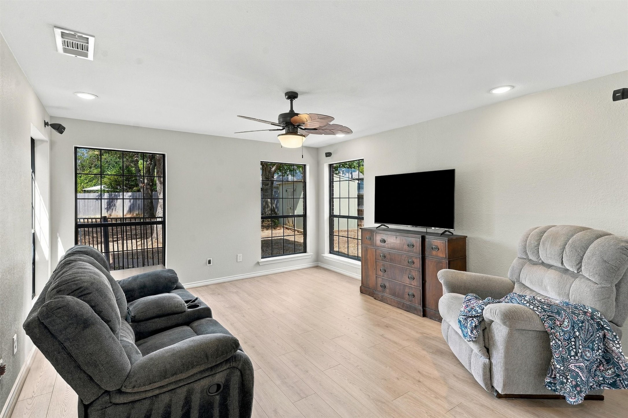 Furnished living room with two recliners, black-grid windows, and a ceiling fan.