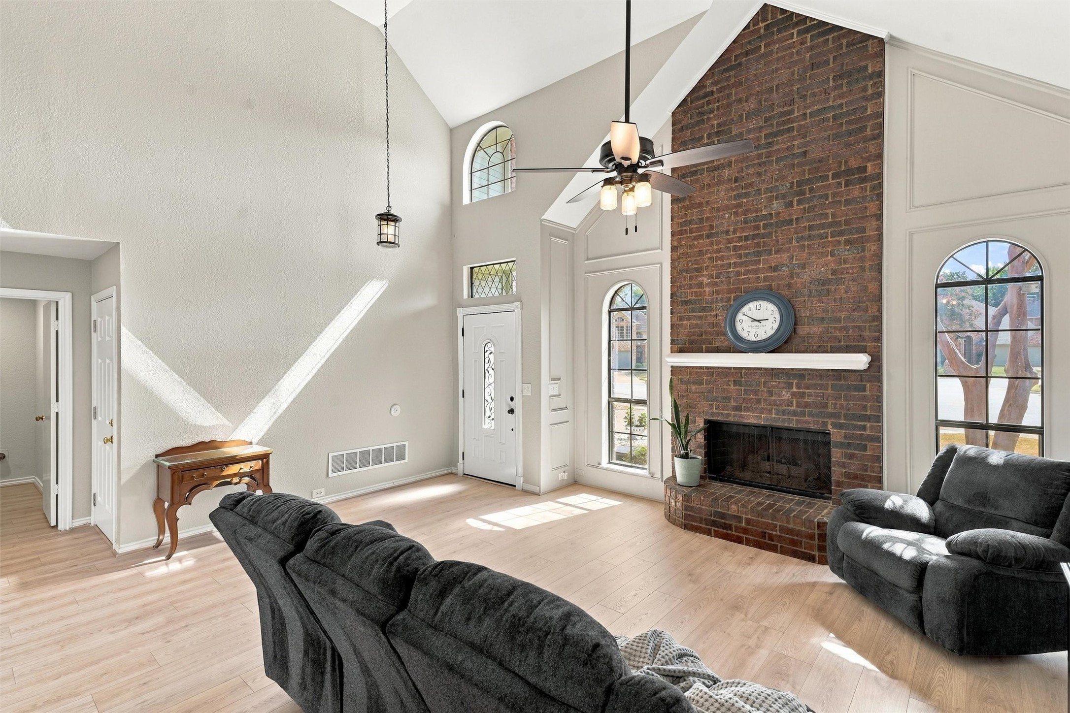 Living room with vaulted ceiling, brick fireplace, arched windows, and dark gray sofas.