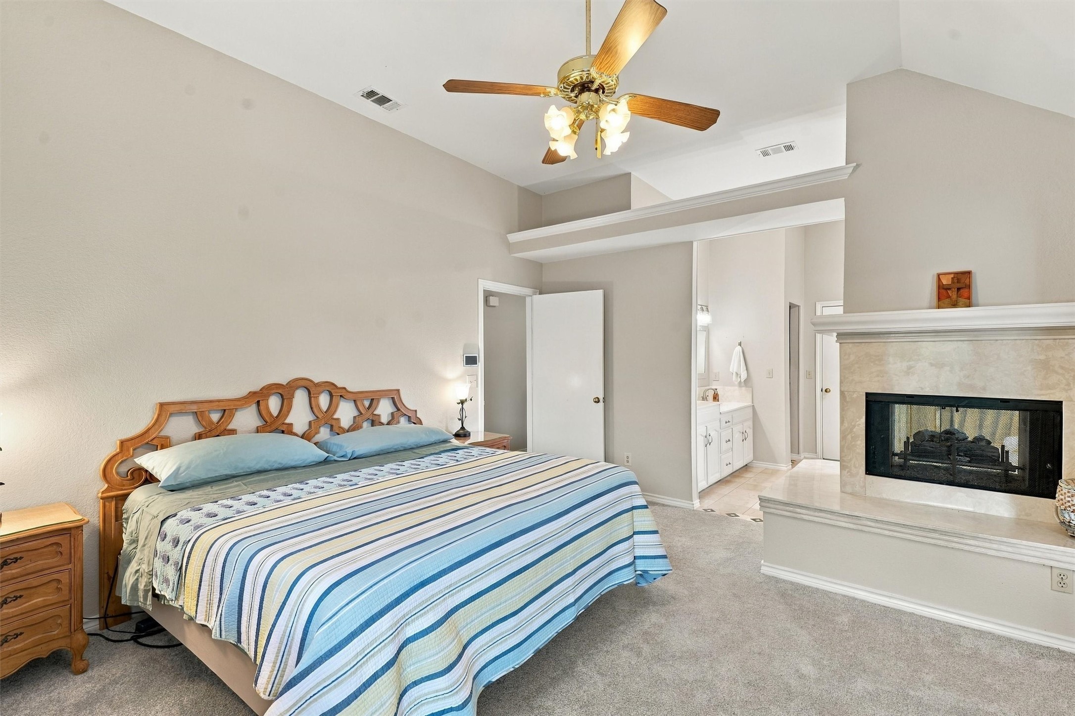 Bedroom with striped blue bedding, a carved wooden headboard, and a large tiled fireplace.