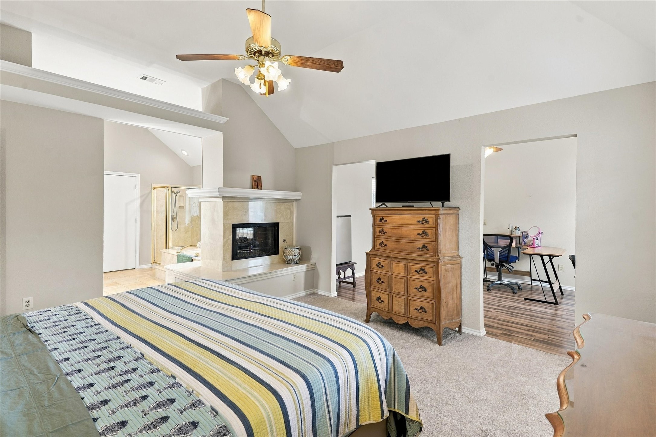Bedroom with a striped bedspread, vaulted ceiling, fireplace, and adjoining desk area.