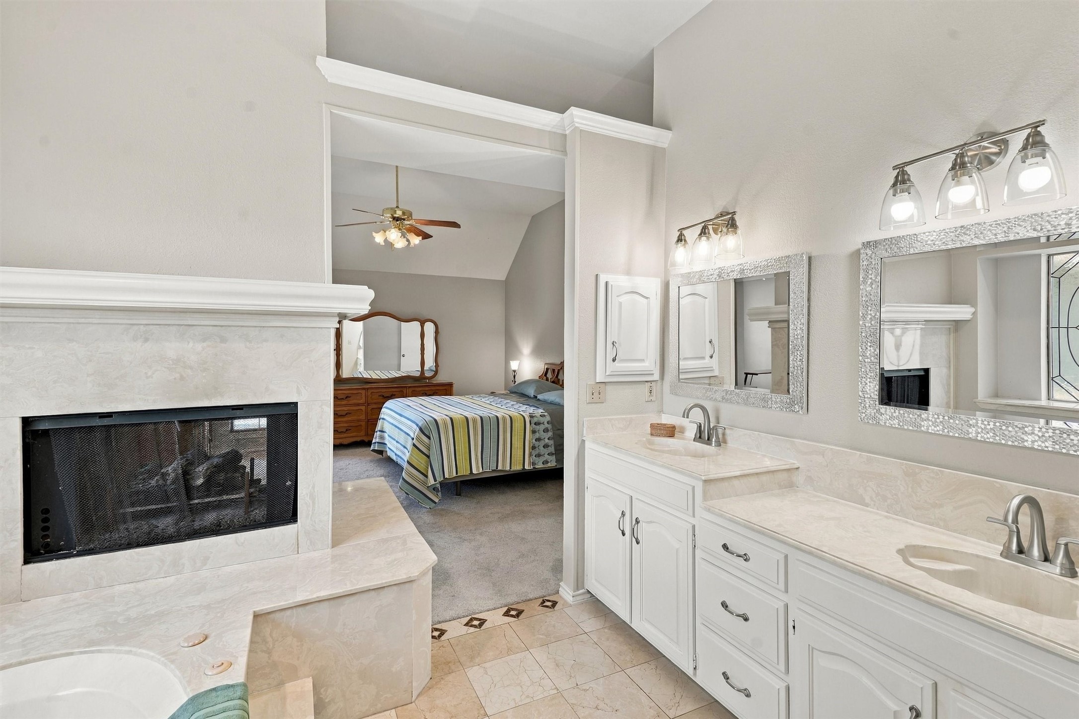 Primary bathroom with double vanity and fireplace opening onto a bedroom.