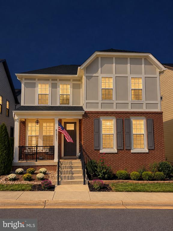 Two-story gray-and-brick home with an American flag and warmly lit windows at dusk.