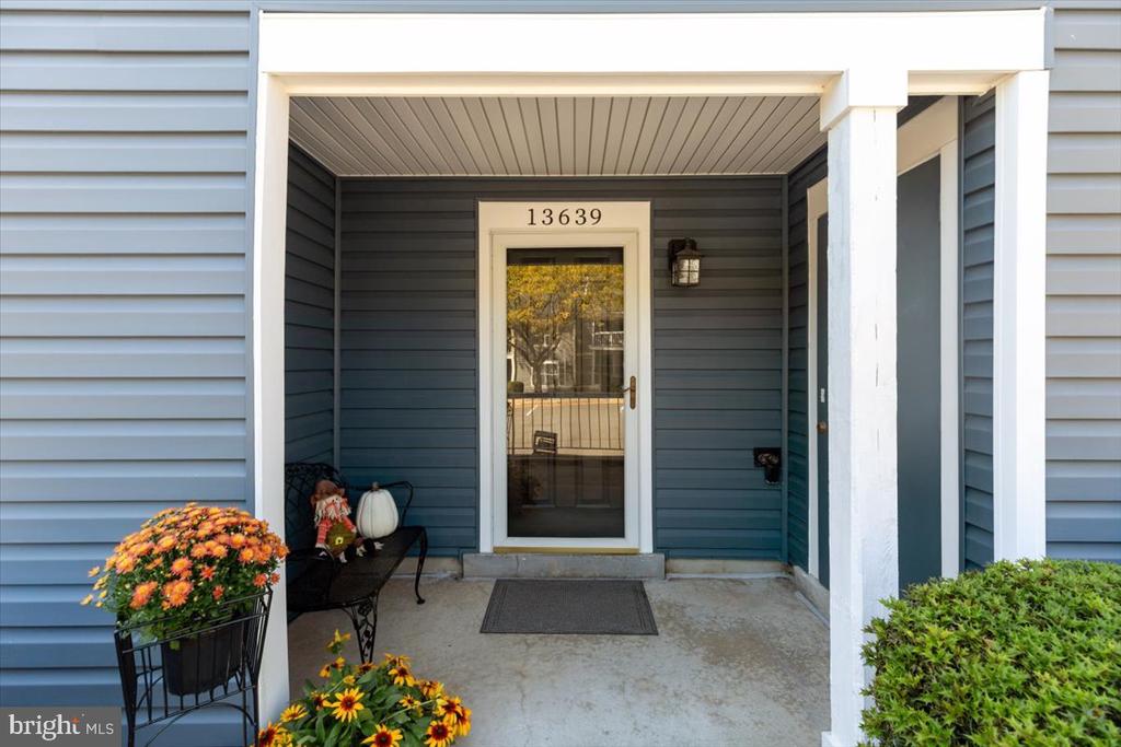 Covered front entry with blue-gray siding, a glass door marked 13639, and orange flowers.