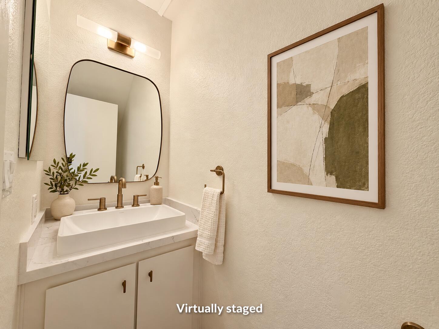 Bathroom vanity with a vessel sink, brass fixtures, asymmetrical mirror, and framed abstract artwork.