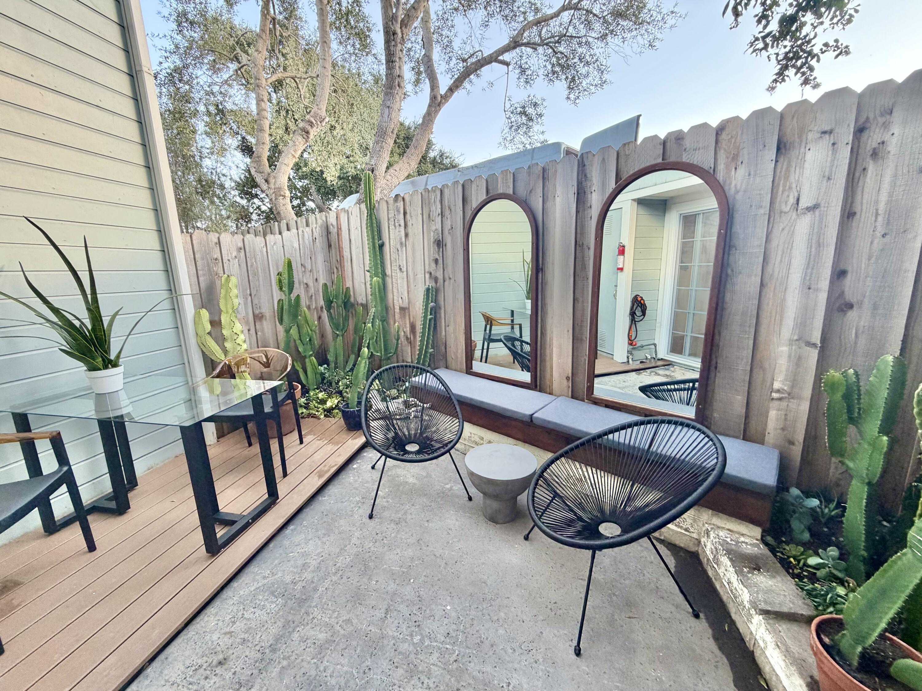 Private courtyard patio with black lounge chairs, a raised wood deck, cacti, and arched mirrors on a wooden fence.
