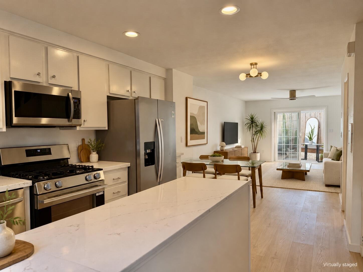 Open-plan kitchen and living area with a long white island, stainless steel appliances, and glass patio doors.