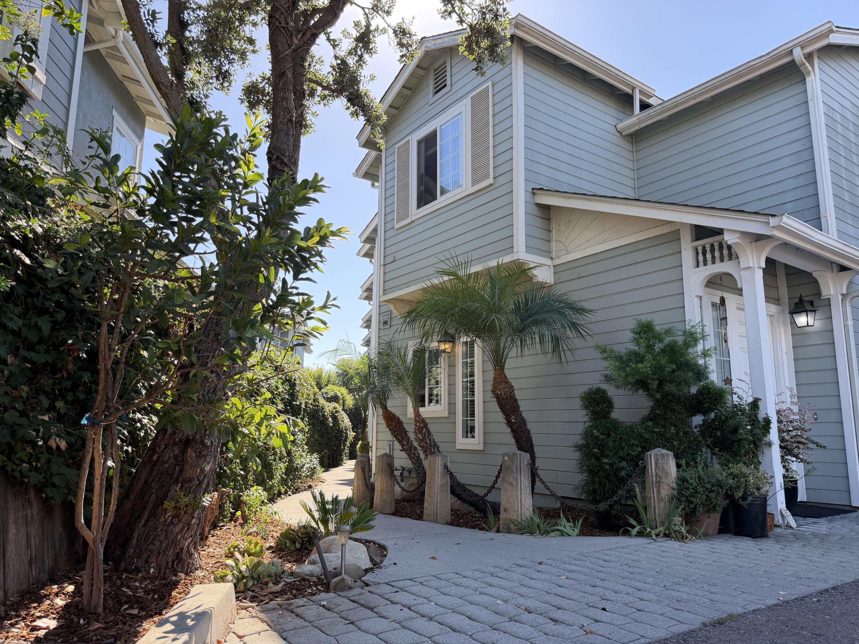 Pale blue-gray home with a white-trimmed porch, palms, and a paved driveway.