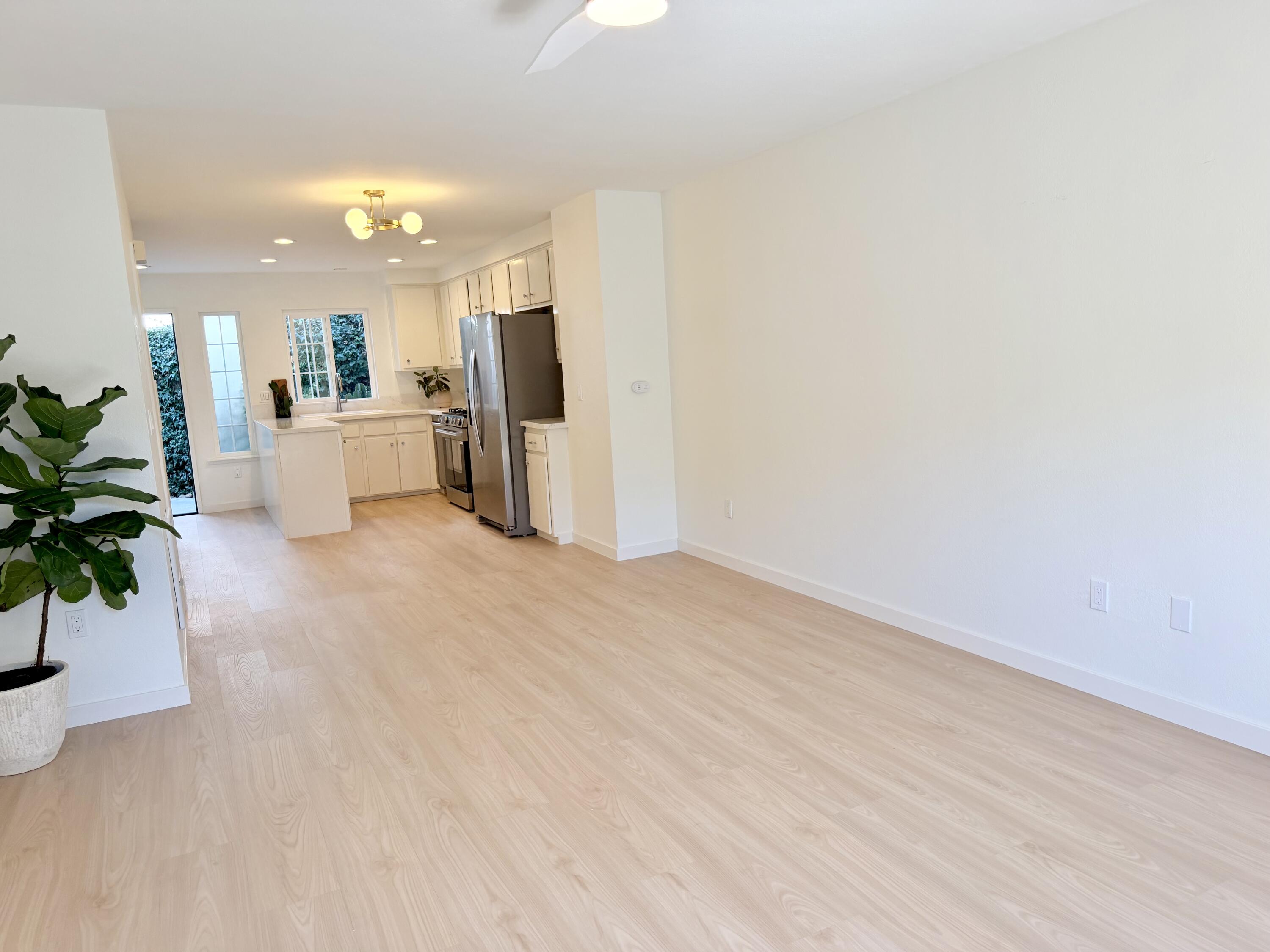 Open living area with pale wood floors and a white kitchen with stainless steel appliances.