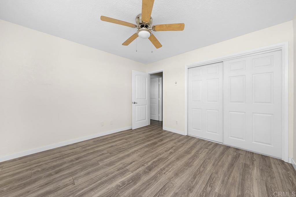 Empty bedroom with wood-look flooring, a ceiling fan, and white closet doors.