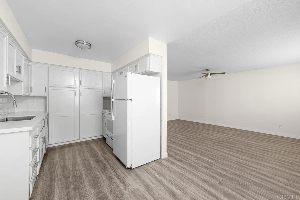 White kitchen with matching appliances opens onto an empty living area with wood-look floors.