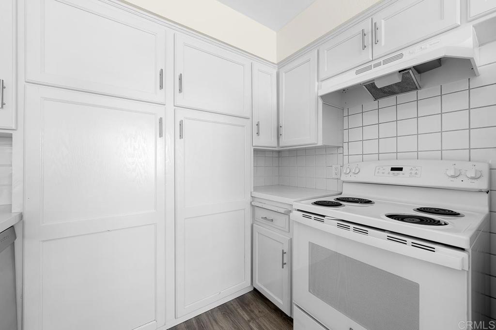 Kitchen with white paneled cabinets, a coil-burner range, tiled backsplash, and dark wood-look flooring.