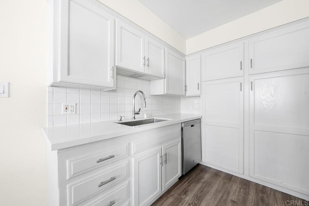 Kitchen with white paneled cabinets, tile backsplash, stainless-steel dishwasher, and wood-look flooring.