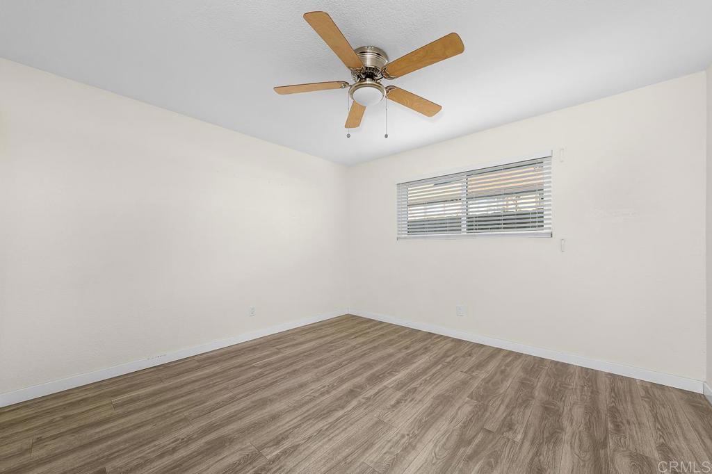 Empty bedroom with wood-look flooring, a ceiling fan, and a window with blinds.