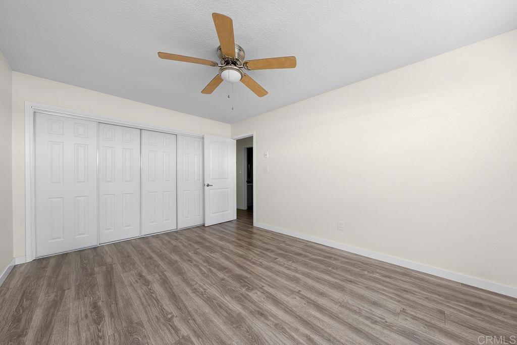 Empty bedroom with gray wood-look flooring, white closet doors, and a ceiling fan.