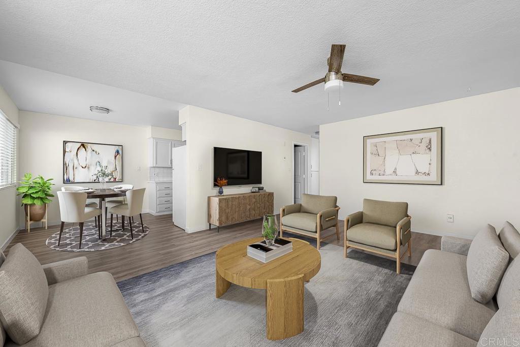 Staged living and dining room with gray seating, a round wood coffee table, and a ceiling fan.