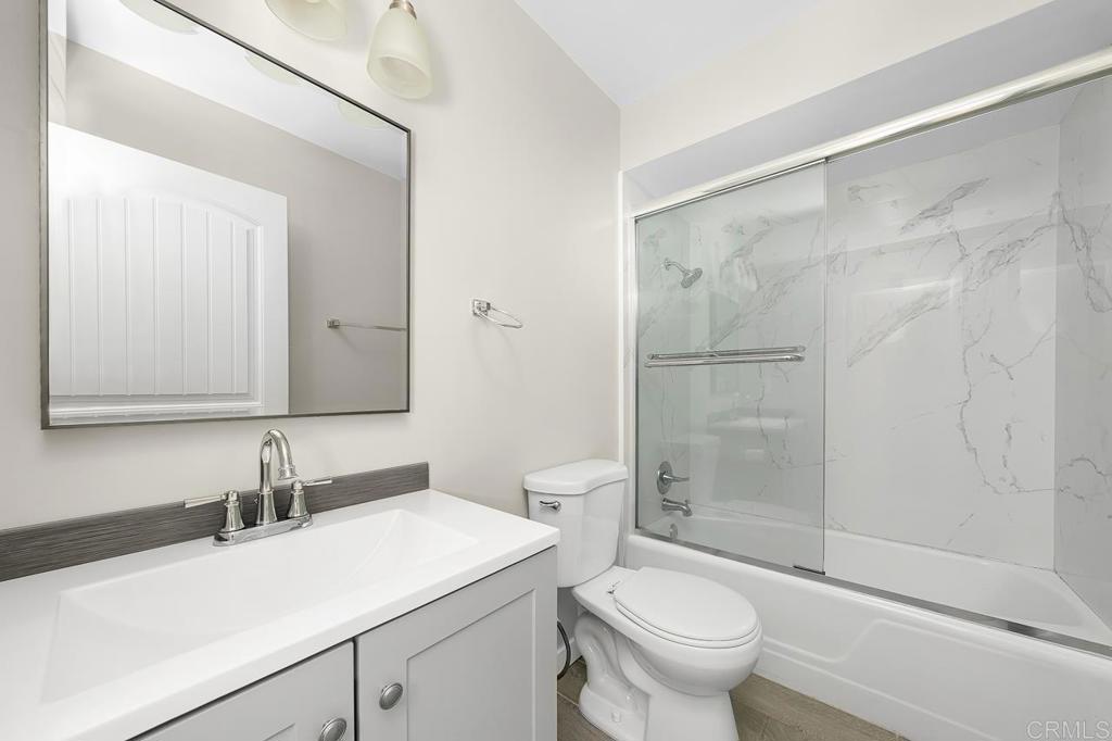 Bathroom with white vanity, sliding glass shower doors, and marble-look wall panels.