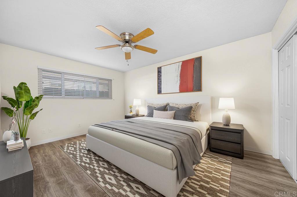 Staged bedroom with gray bedding, a patterned rug, abstract art, and a ceiling fan.