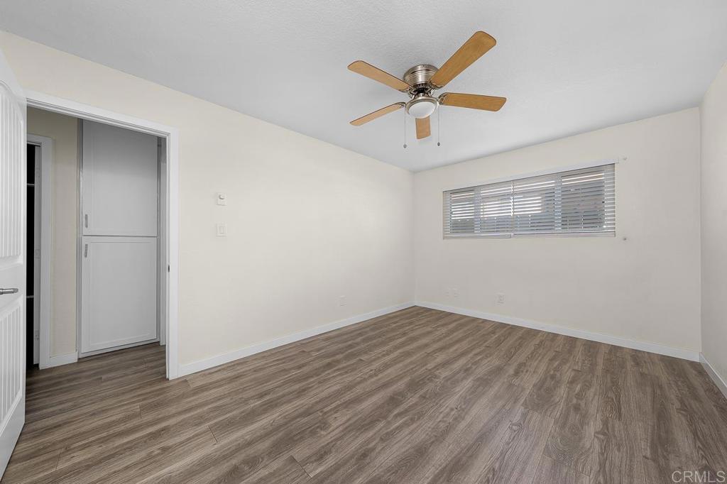 Empty room with wood-look floors, a ceiling fan, and a wide window with blinds.