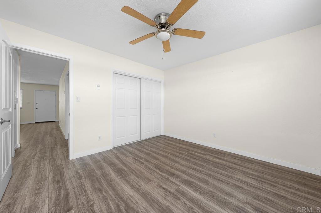 Empty bedroom with gray wood-look flooring, double closet doors, and a wood-bladed ceiling fan.