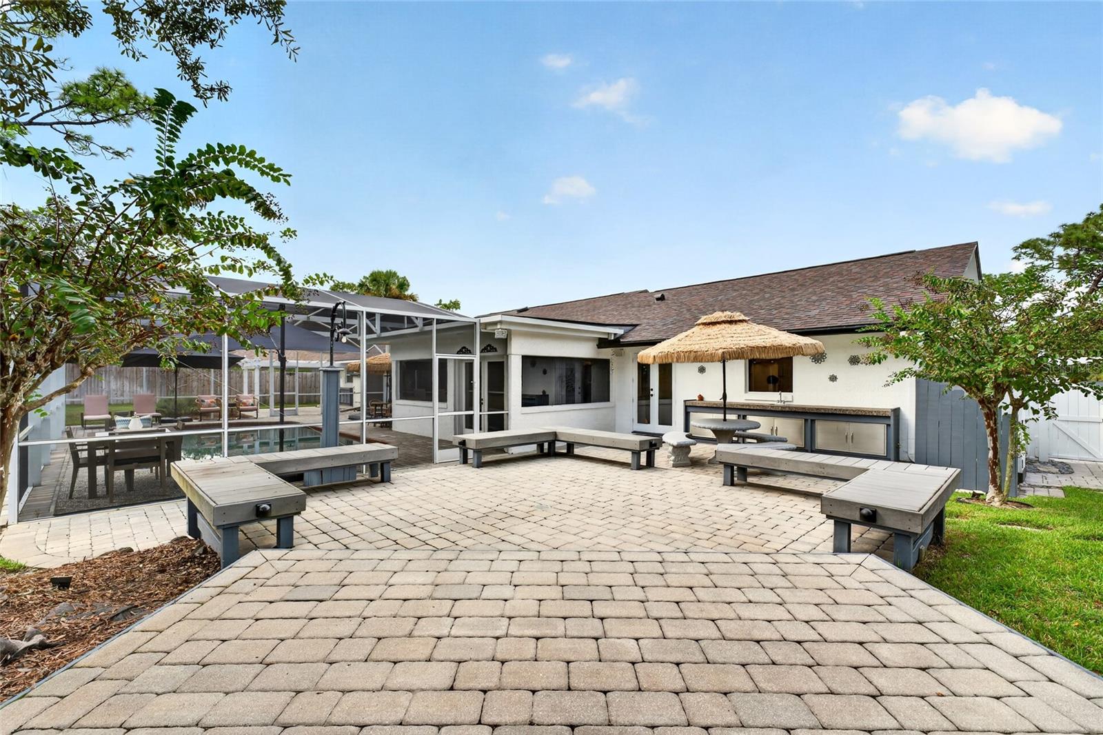 Backyard patio with built-in benches, an outdoor kitchen, and a screened pool enclosure.