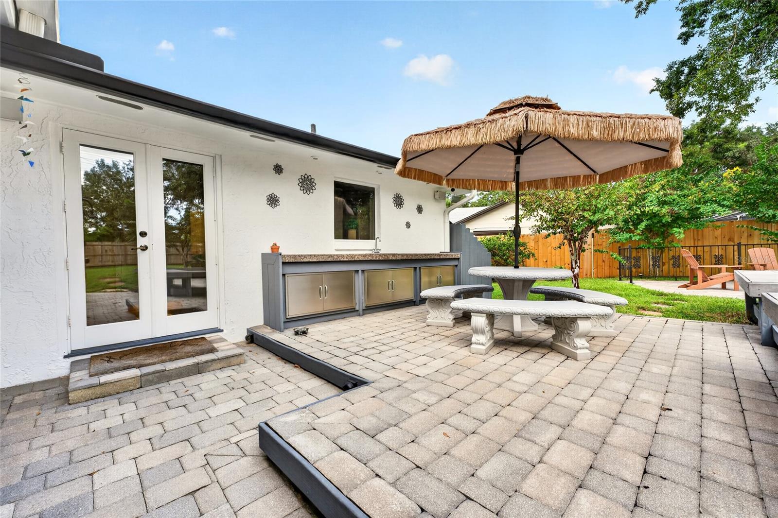 Backyard patio with a built-in outdoor kitchen and thatched umbrella over a stone table and benches.