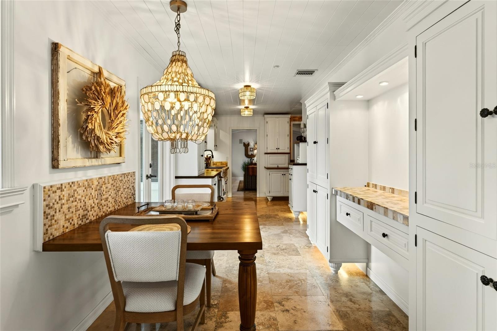 Dining area with a wood table, ornate chandelier, white built-in cabinetry, and stone flooring.