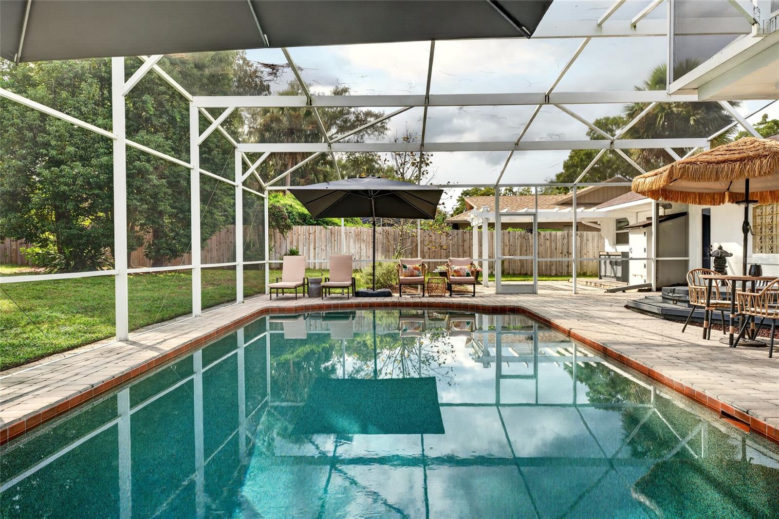 Backyard pool beneath a screened enclosure, with lounge seating and an outdoor dining area.