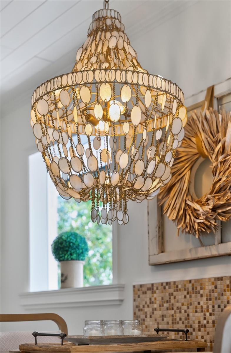 Ornate chandelier hangs above a kitchen with a mosaic tile backsplash and bright window.