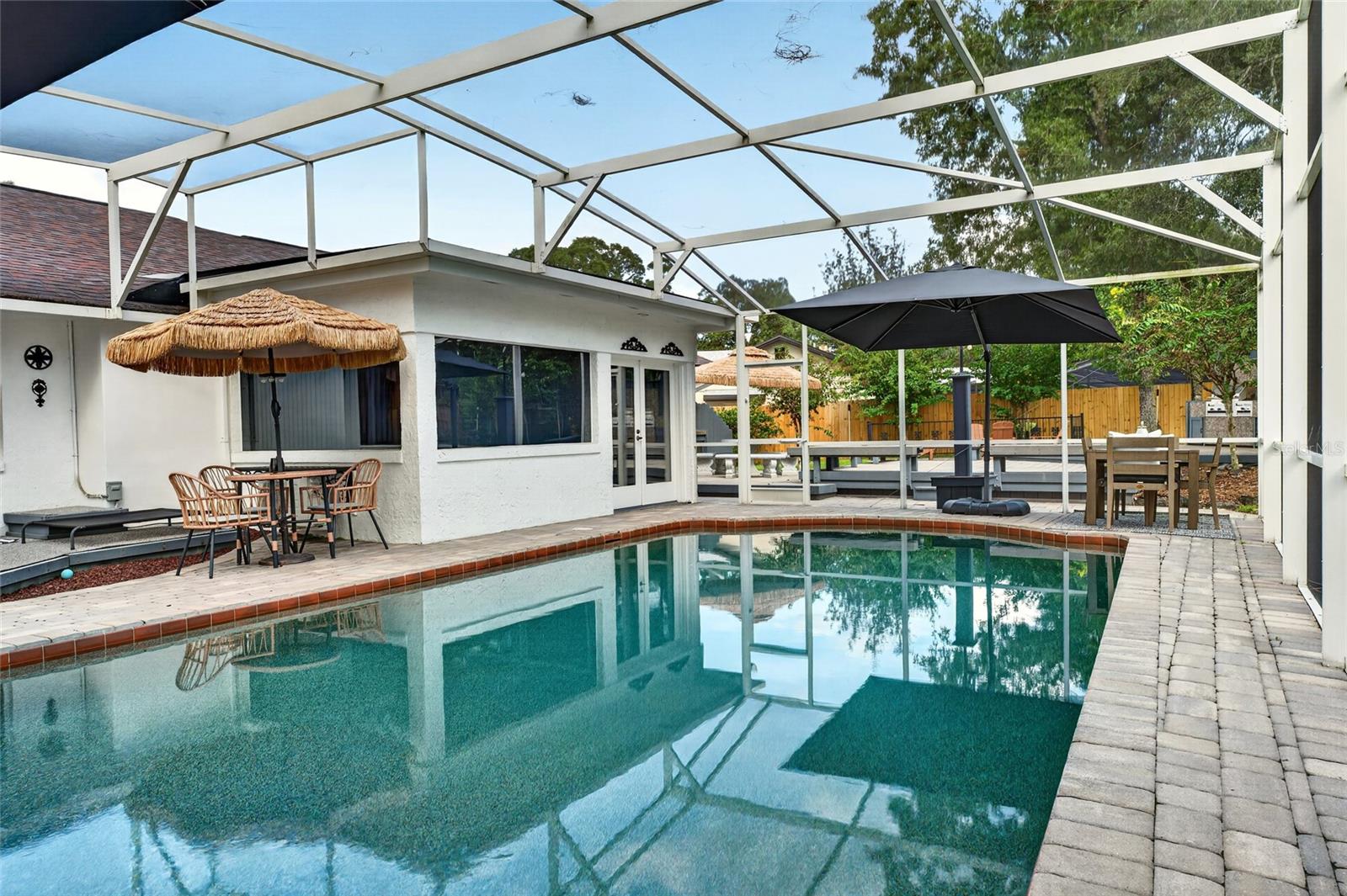 Backyard pool under a screened enclosure, with patio dining areas and shade umbrellas.