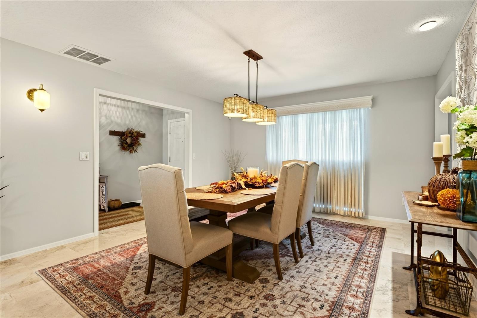 Dining room with a wooden table, upholstered chairs, woven pendant lights, and a large curtained window.