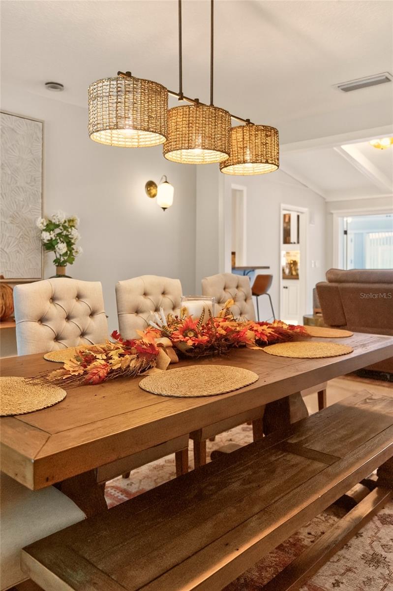 Dining area with a long wooden table, bench, tufted chairs, and three woven pendant lights.