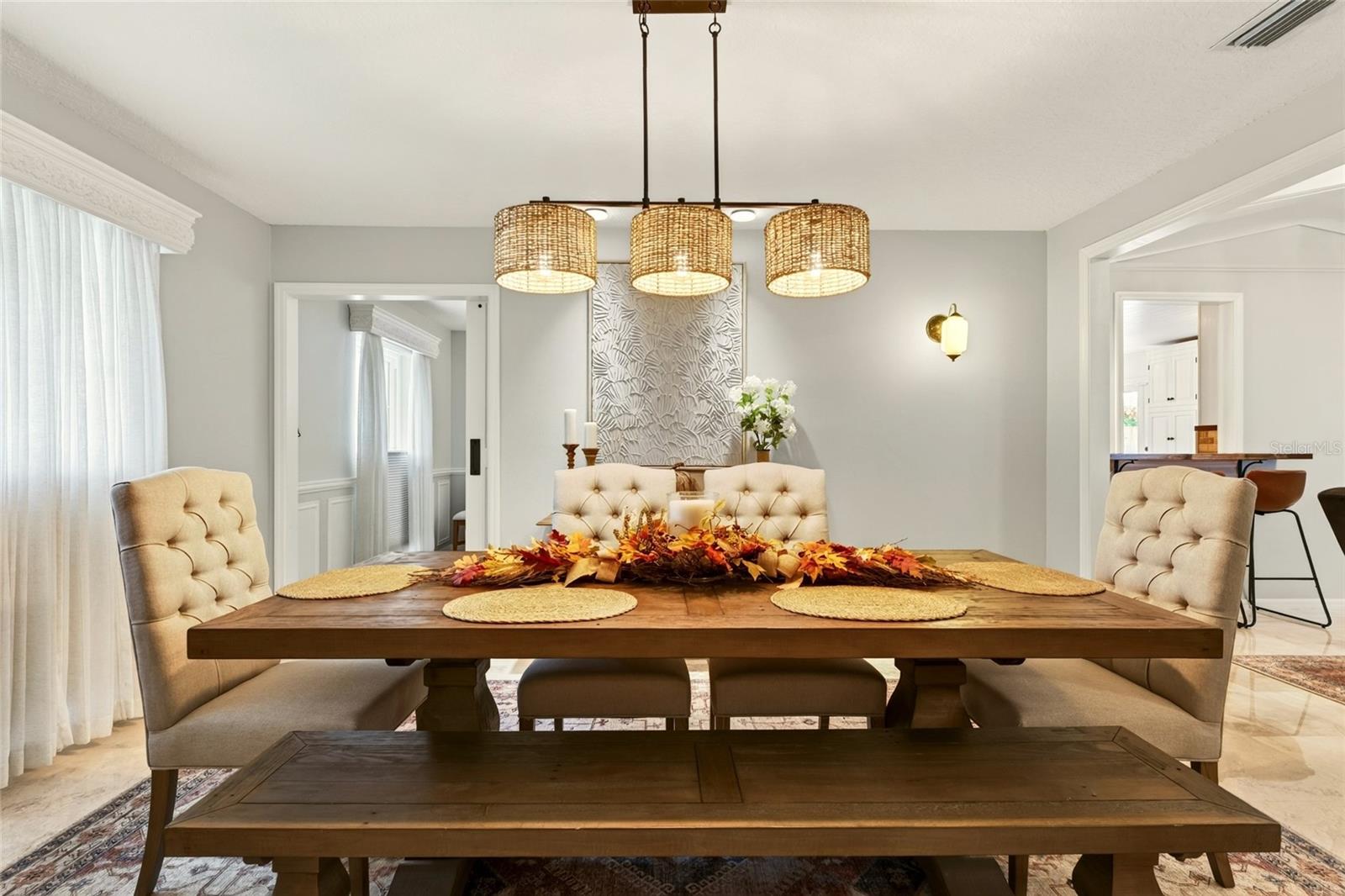 Dining room with a rustic wood table, upholstered chairs, and three woven pendant lights.