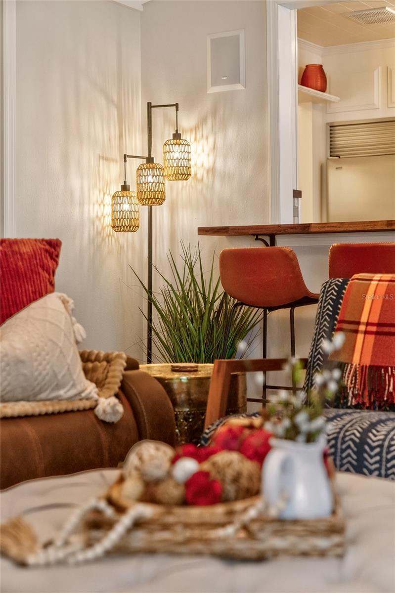 Staged living room with brown sofa, patterned cushions, pendant lamps, and bar seating.
