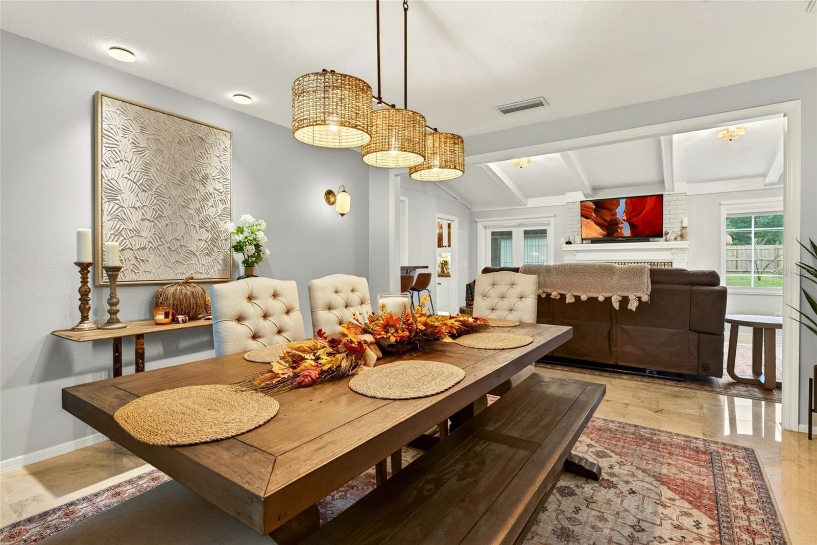 Dining room with a rustic wood table and woven pendant lights opening into a living room.