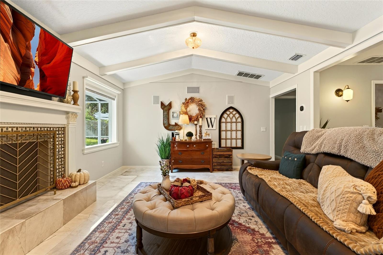 Living room with vaulted ceiling, tiled fireplace, leather sofa, and round ottoman.
