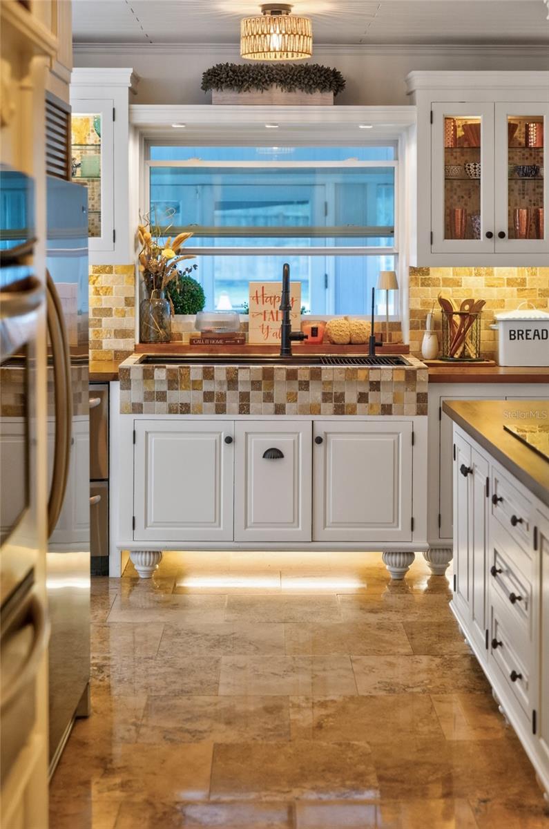 Kitchen with white cabinets, mosaic tile around the sink, and tan stone flooring.