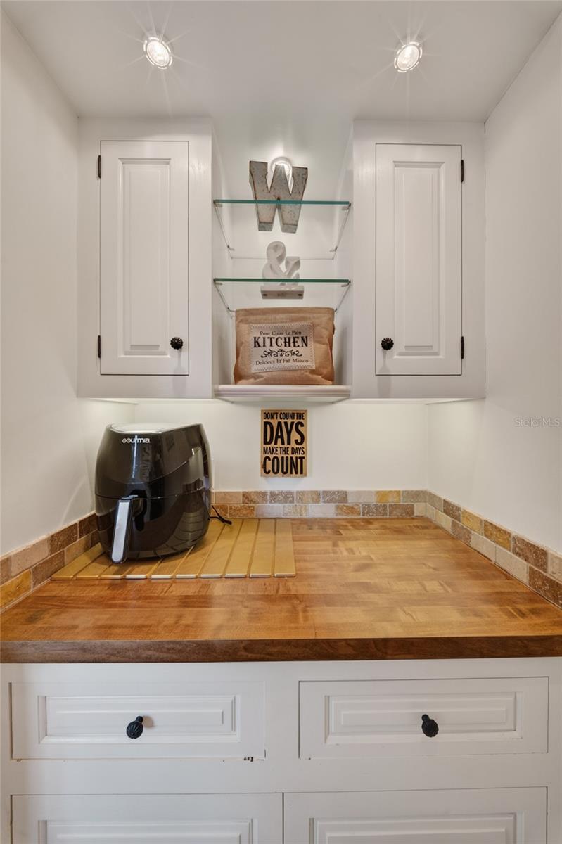 Kitchen counter with white cabinets, glass shelves, tiled backsplash, and a black air fryer.