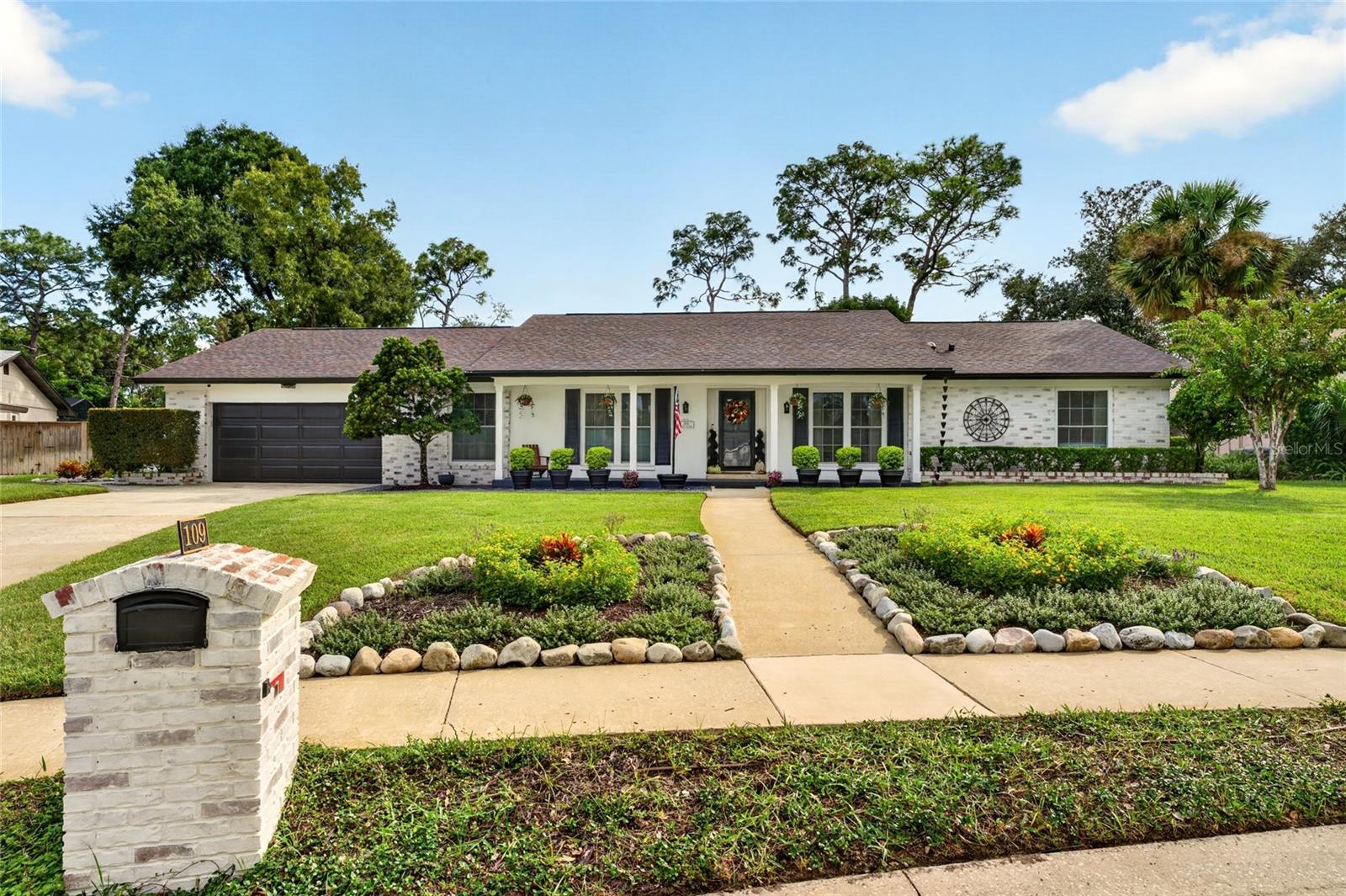 Single-story white brick home with a two-car garage, landscaped front garden, and stone mailbox marked 109.